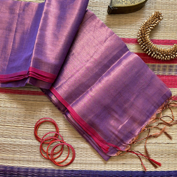 Completely plain tissue by cotton saree in copper and mauve two tone and red slub border. The pallu has golden tassels. 
Does not come with a blouse. 